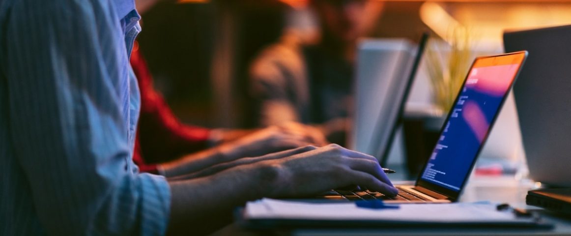 Male entrepreneur working late in office. He is sitting, using his laptop to try to solve problem with code.