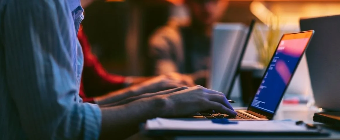Male entrepreneur working late in office. He is sitting, using his laptop to try to solve problem with code.