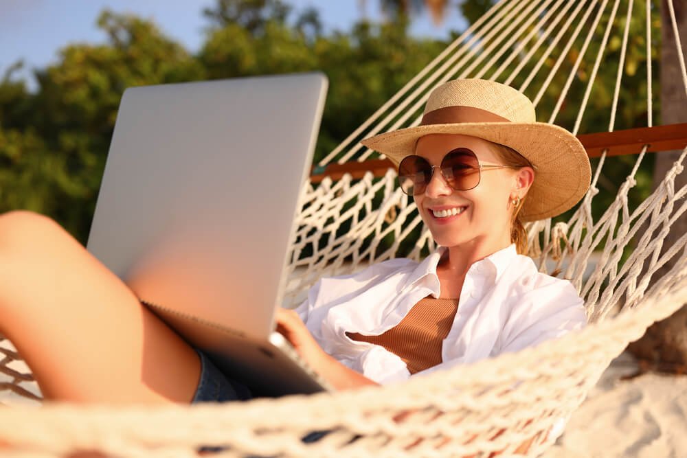 Kobieta leżąca na hamaku korzysta z laptopa do pracy zdalnej